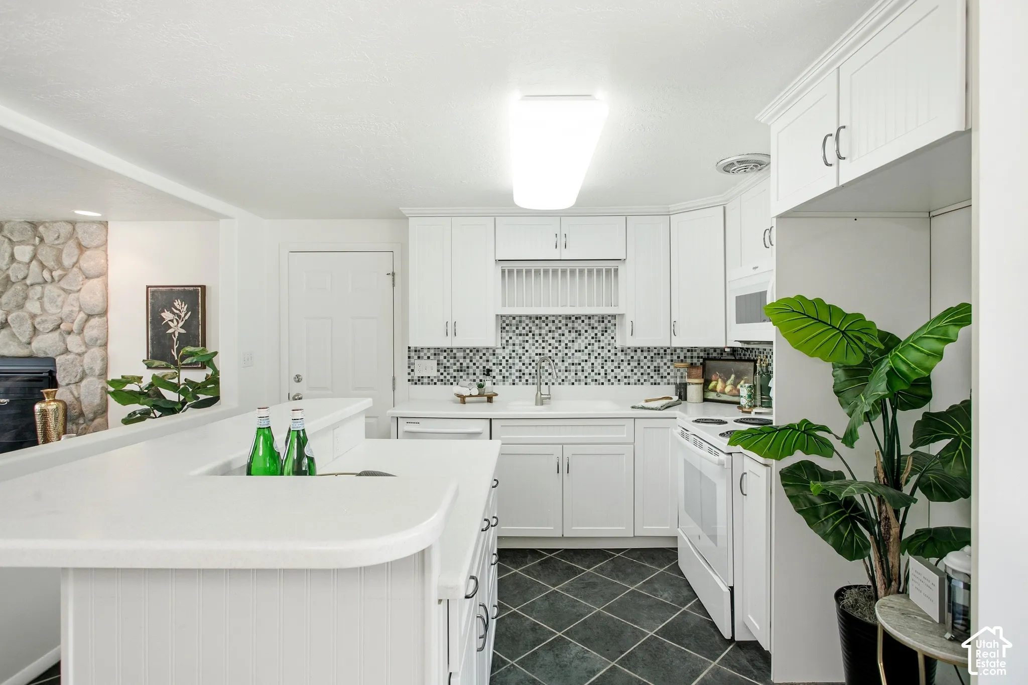 White cabinetry with panel doors, mosaic tile backsplash, black tile flooring, and white countertops