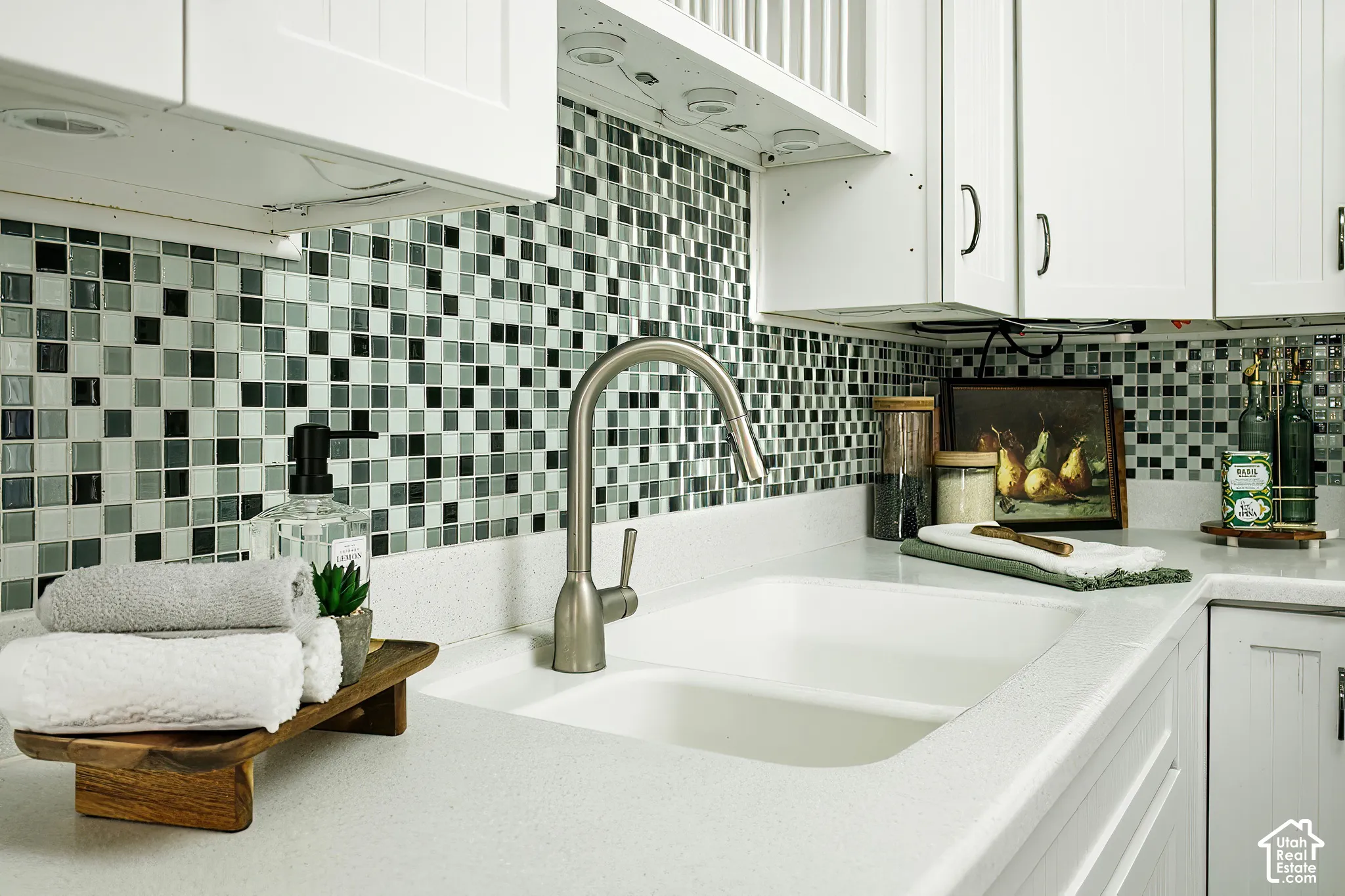 White shaker-style cabinetry, mosaic tile backsplash, dual-basin sink, brushed nickel faucet, and white countertops