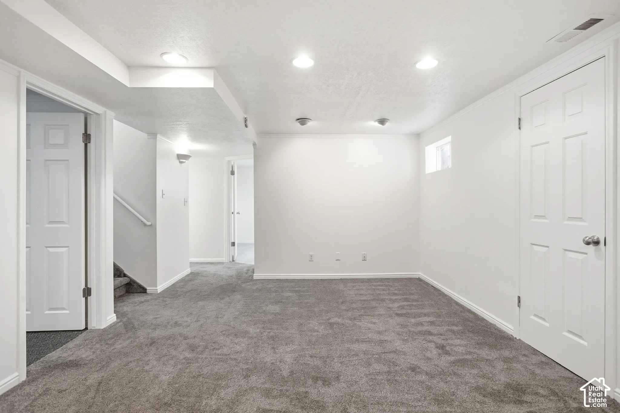 Spacious room with gray carpet flooring, white walls, recessed ceiling lighting, and a white paneled door