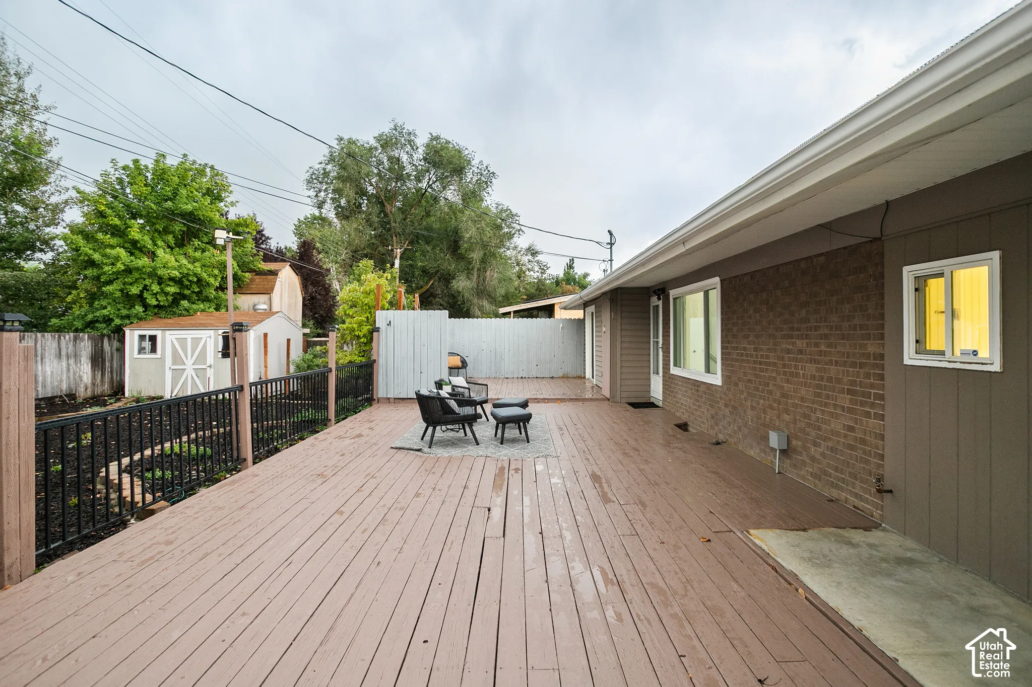 Expansive outdoor deck with a dark wood-finish surface, brick and siding exterior, and a built-in storage shed