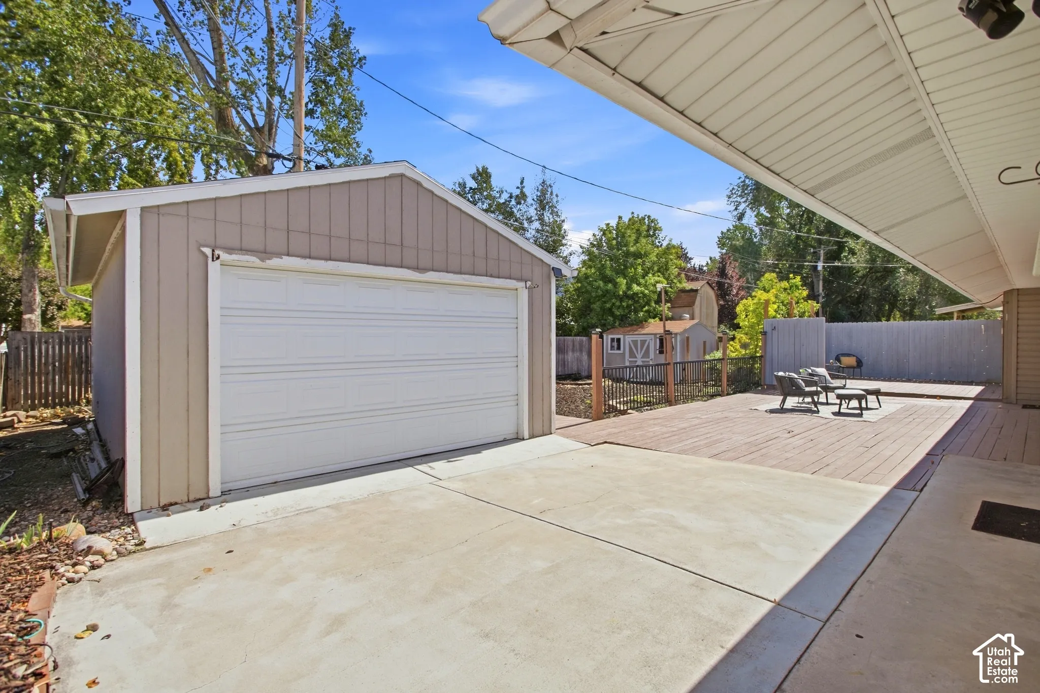 Detached garage with a roll-up door, concrete patio surface, extended wood-finish decking, and a large patio/deck area