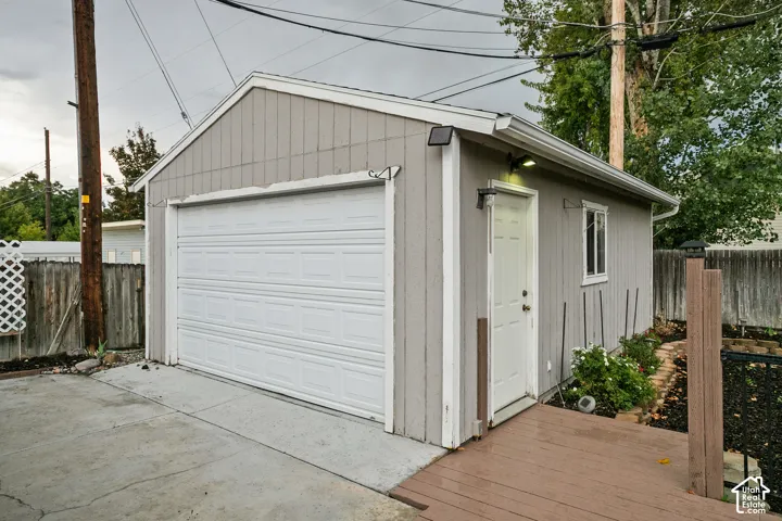 Detached garage with a paneled overhead door, a side entry door, and a wood-finish deck