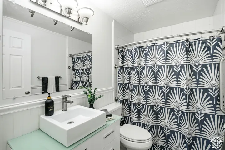 Bathroom featuring a vessel sink, single-handle faucet, wainscoting, and a shower with a grab bar