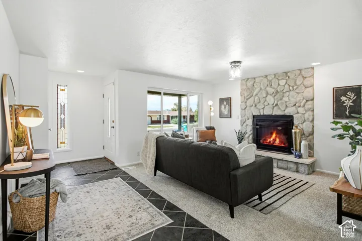 Stone-clad fireplace with hearth, large glass sliding door, decorative front door with side light, recessed lighting, and mixed flooring