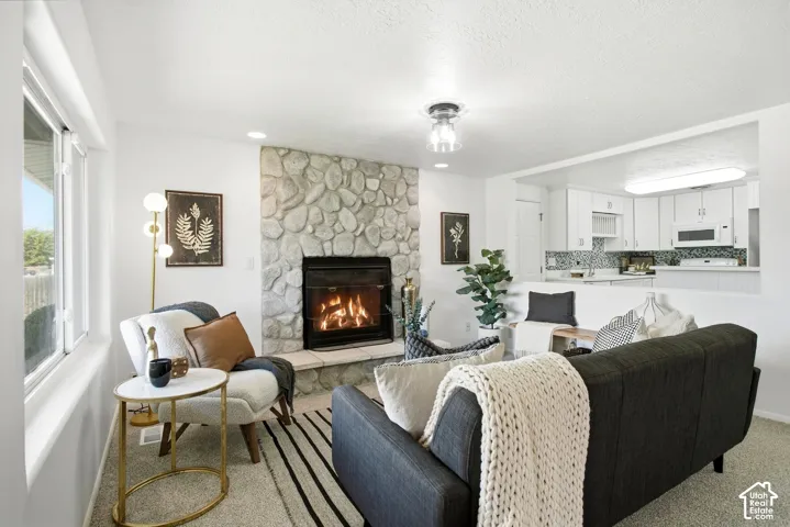 Stone-clad fireplace with hearth, white window frames, recessed lighting, and kitchen pass-through with white cabinetry