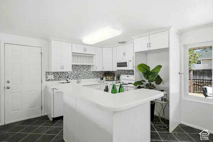 White cabinetry with beadboard paneling, mosaic tile backsplash, solid surface countertops, and dark square tile flooring