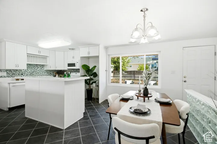 Kitchen and dining area featuring white cabinetry, a kitchen island with a white countertop, a mosaic tile backsplash, and dark diamond-patterned floor tiles