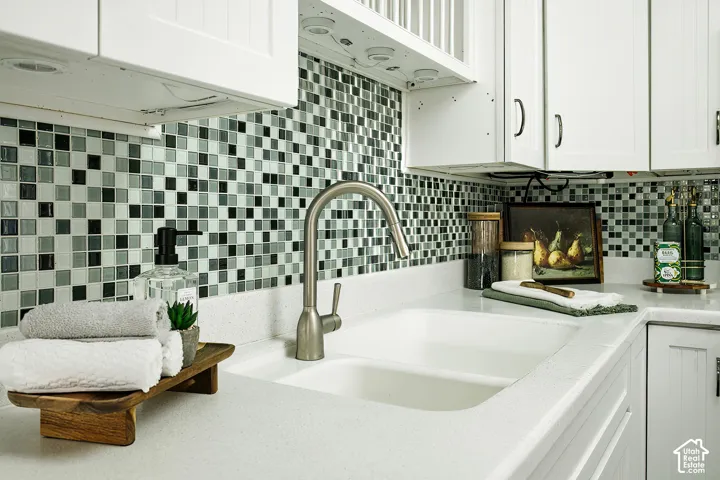White shaker-style cabinetry, mosaic tile backsplash, dual-basin sink, brushed nickel faucet, and white countertops