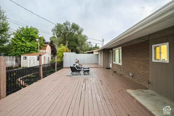 Expansive outdoor deck with a dark wood-finish surface, brick and siding exterior, and a built-in storage shed