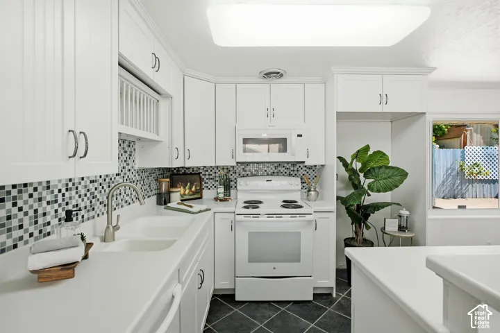 White cabinetry with dark hardware, mosaic tile backsplash, double basin sink with a gooseneck faucet, white built-in appliances, and dark diamond-patterned flooring