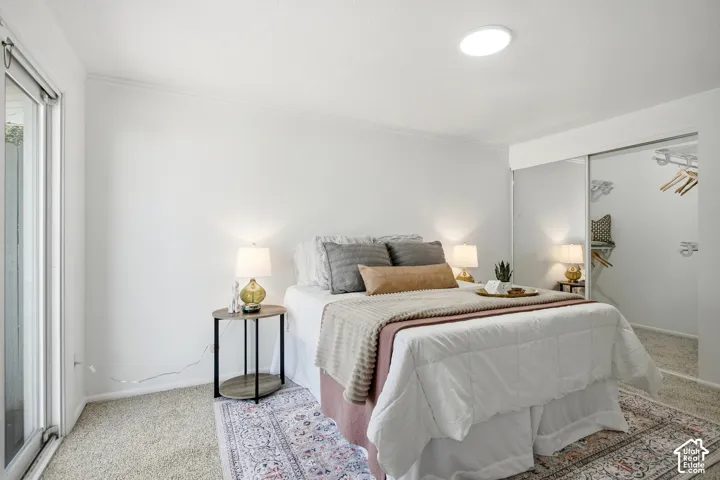 Serene primary bedroom featuring a mirrored accent wall, recessed ceiling lighting, dual bedside tables with task lamps, glass sliding door access to outdoor space, and layered area rugs over neutral carpeting
