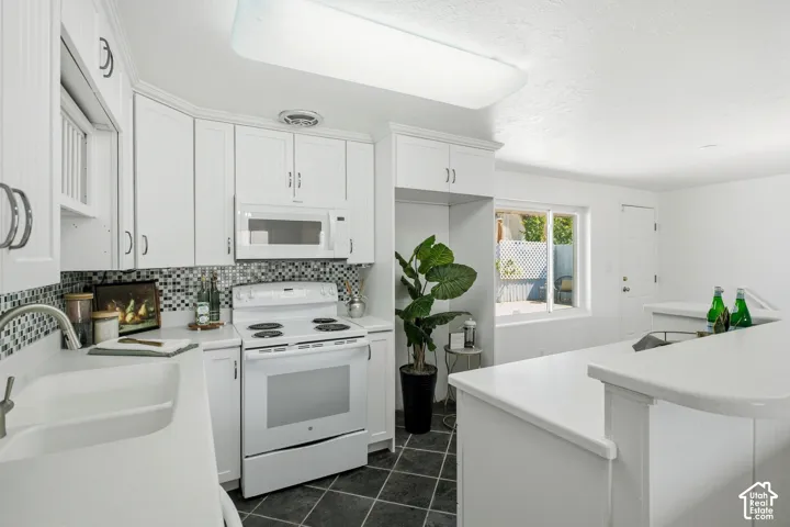 White cabinetry, white appliances, mosaic tile backsplash, built-in microwave, and dark tile flooring