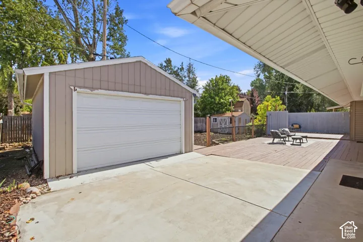 Detached garage with a roll-up door, concrete patio surface, extended wood-finish decking, and a large patio/deck area