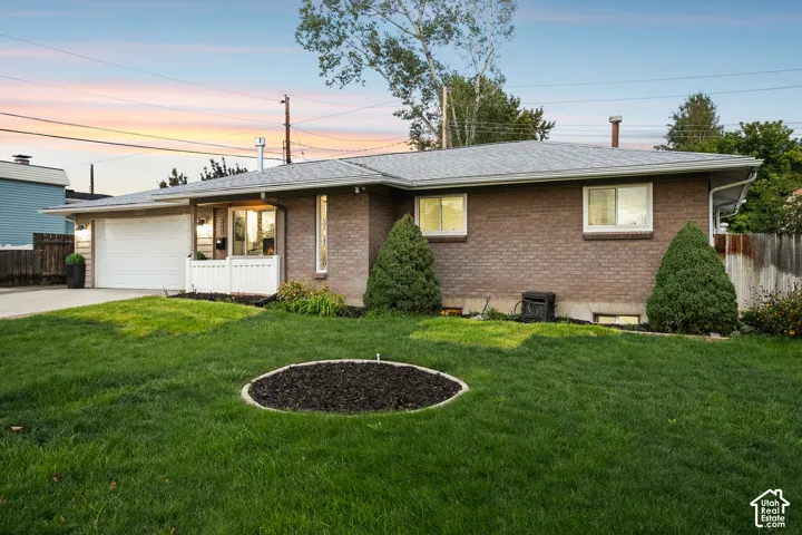 Brick exterior, attached garage, front yard with mature landscaping, bay window, and a gray shingle roof