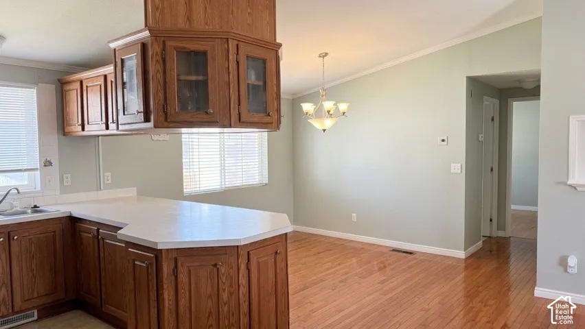 Kitchen with wood cabinetry, light-toned countertops, and a dining area featuring wood-finish flooring and a ceiling-mounted light fixture