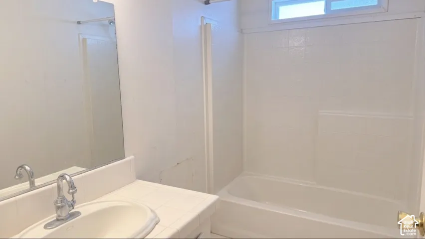 Bathroom featuring a single vanity, tiled countertop, integrated sink, mirrored wall, and a bathtub with a tiled surround