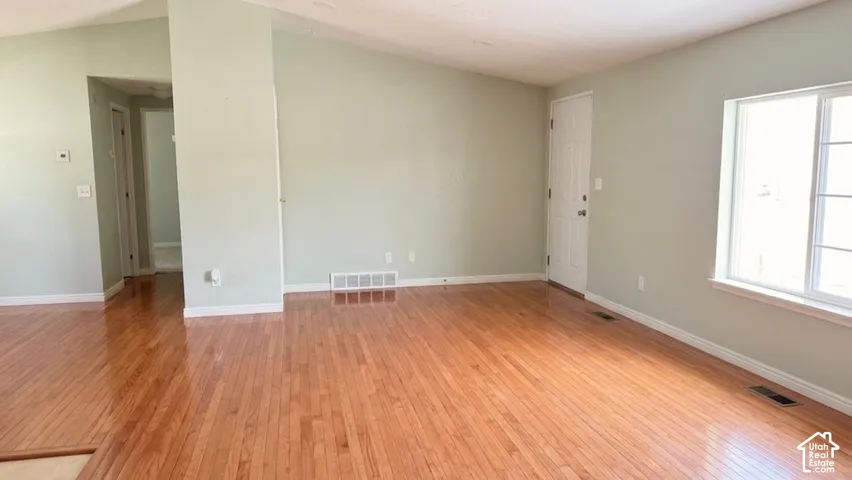 Spacious room featuring wood flooring, a vaulted ceiling, light-toned wall finishes, and a large window