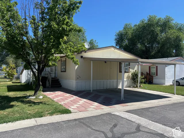 Exterior featuring a covered carport, paved driveway, and manicured lawn