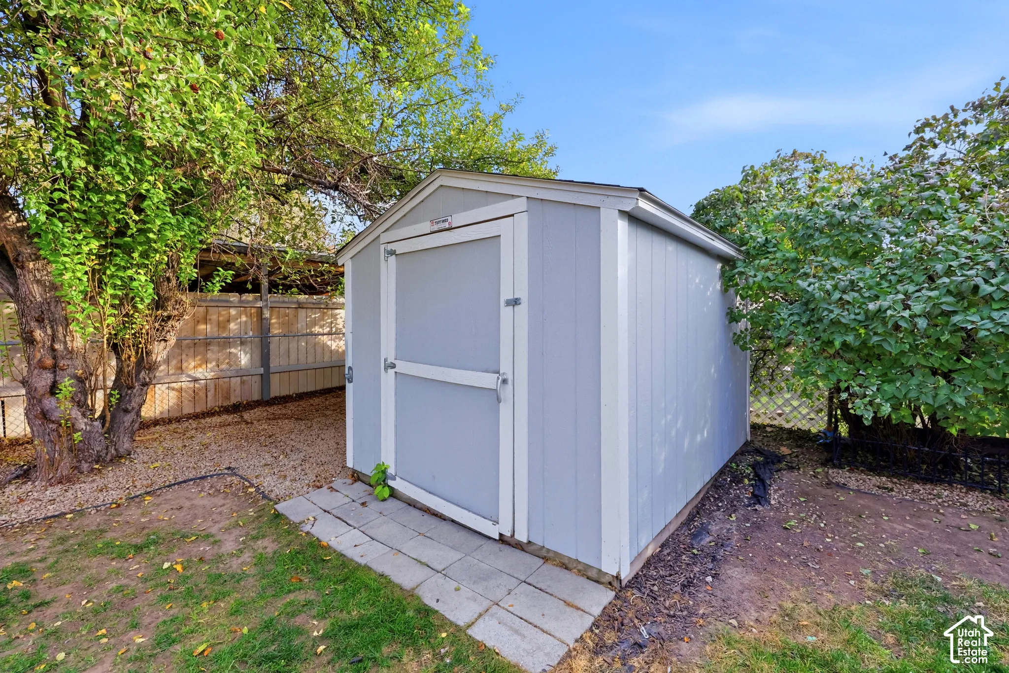 Utility shed with wood panel siding, concrete paver base, and surrounding mature foliage