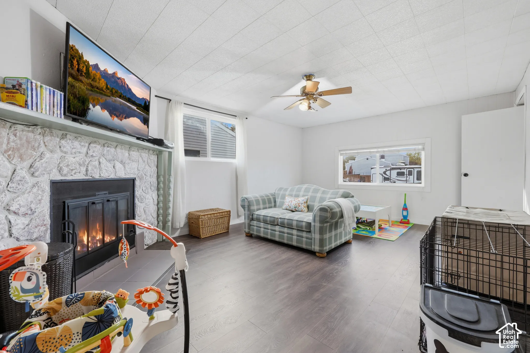 Living space featuring a stone-clad fireplace, wood-finish flooring, and a ceiling fan