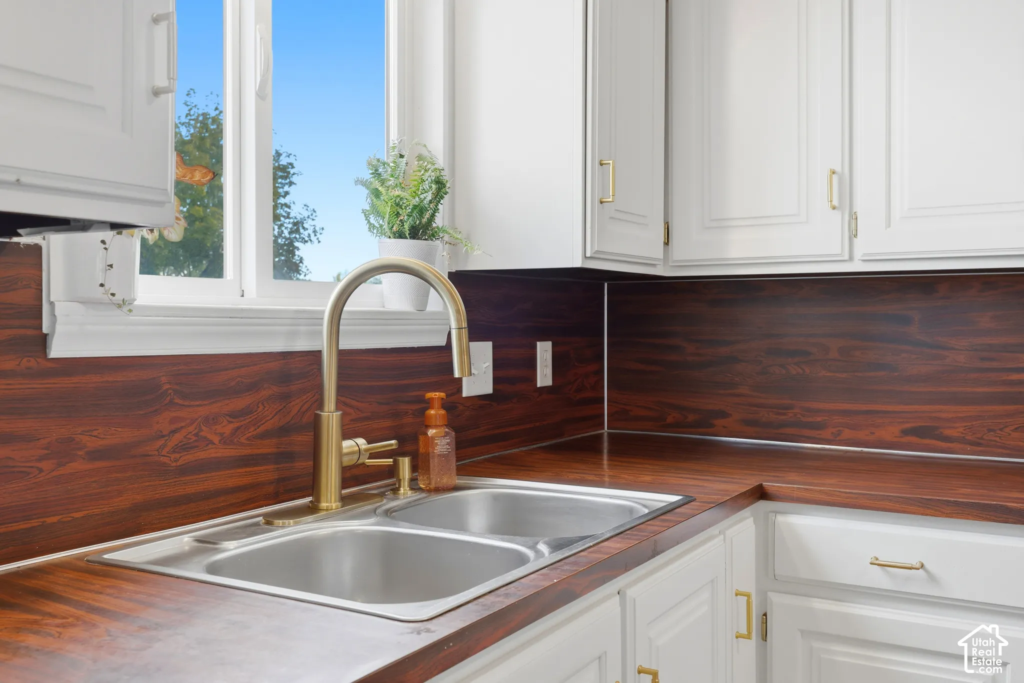 Stainless steel double basin sink with a gold-tone faucet, complemented by wood-finish countertops and backsplash