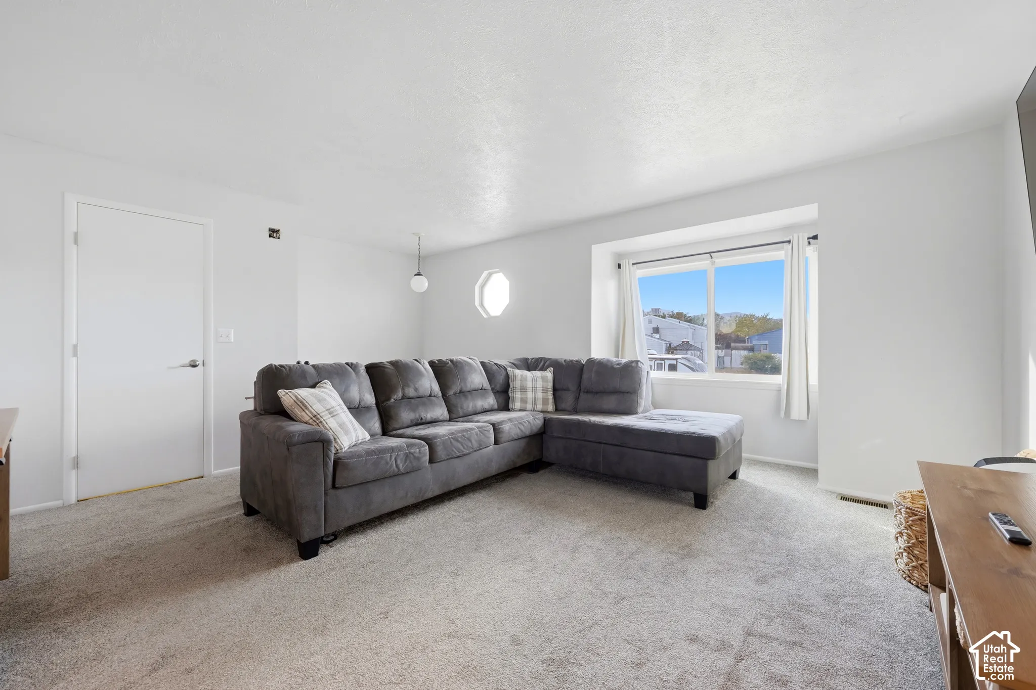 Carpeted flooring, white walls, bay window, round accent window, and a single pendant light fixture