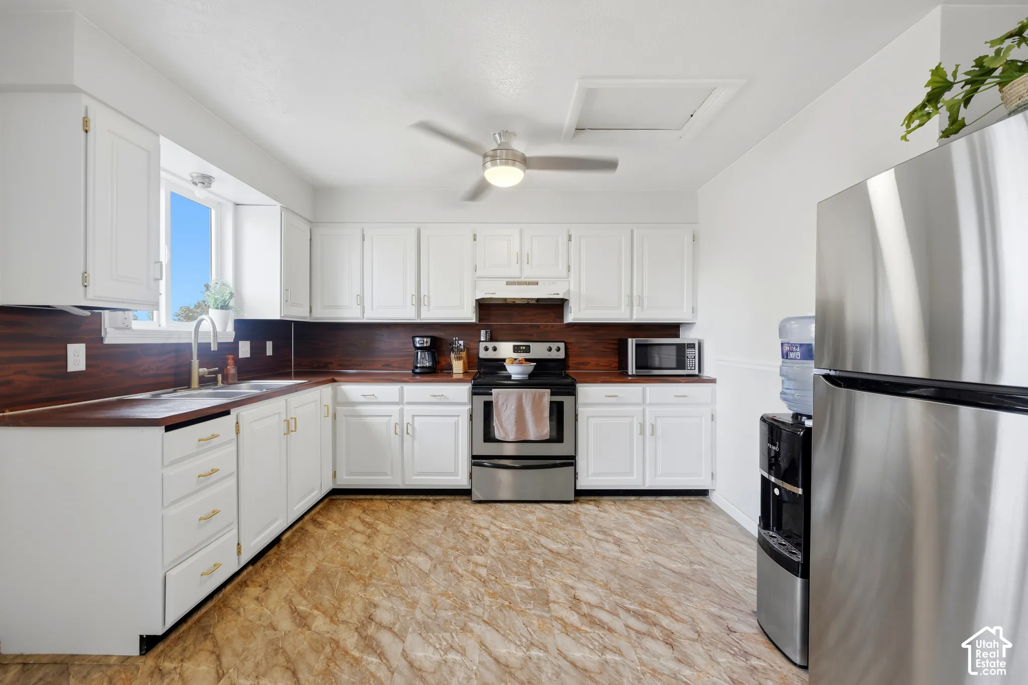 White cabinetry with gold-tone hardware, wood-finish countertops, stainless steel appliances, and a ceiling fan