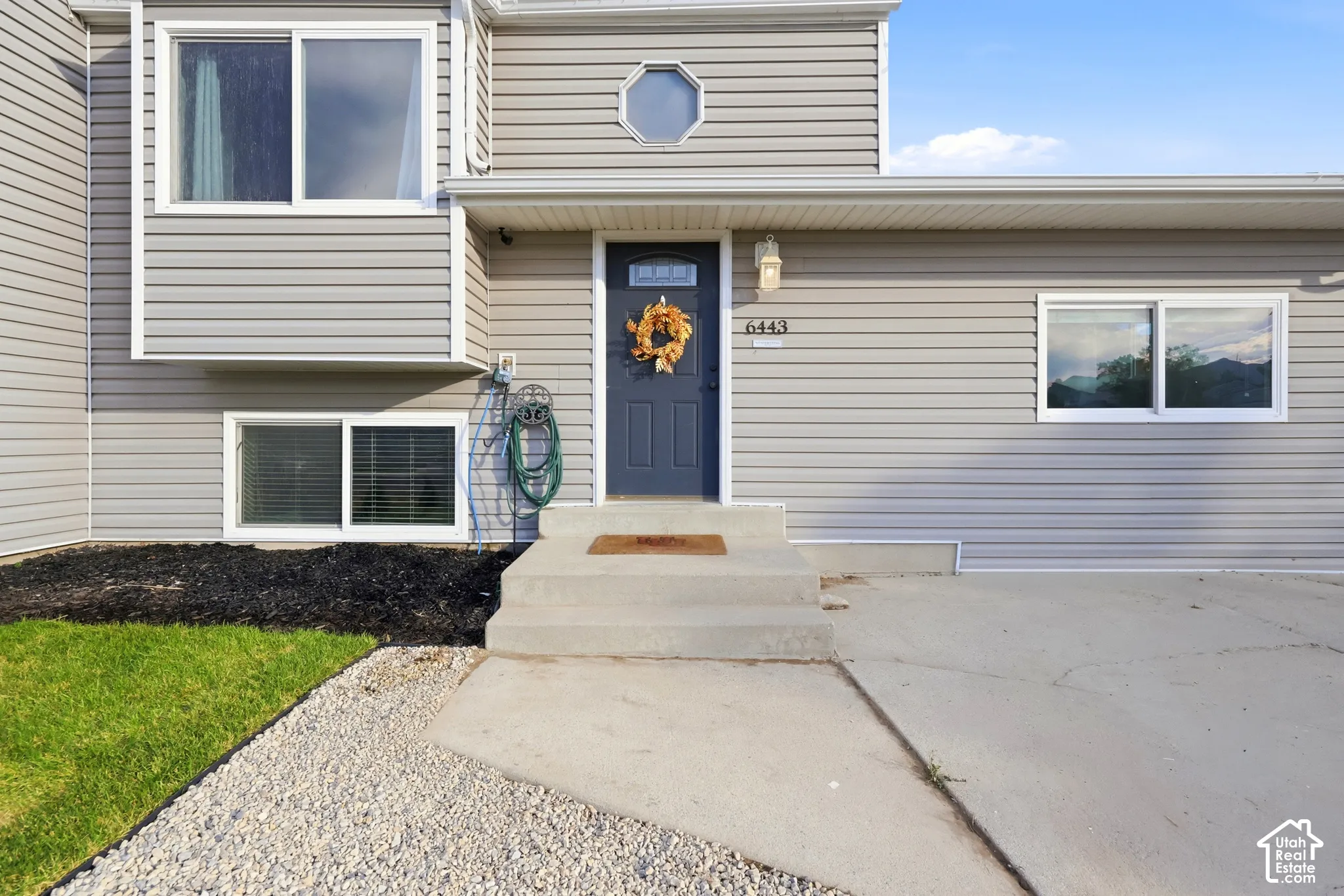 Gray horizontal siding exterior with a dark blue entry door, concrete steps, and a gravel and grass front yard