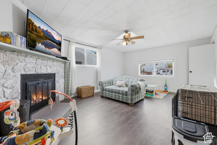Living space featuring a stone-clad fireplace, wood-finish flooring, and a ceiling fan