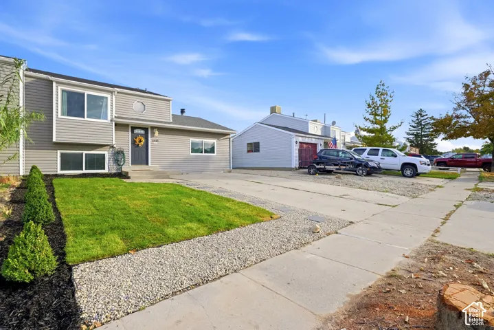 Gray siding exterior with white trim, front entry with transom window, landscaped front yard with green lawn, gravel, and shrubs, and a concrete driveway