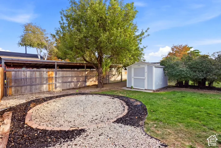 Expansive backyard featuring a manicured lawn, a gravel patio area with wood chip accents, a storage shed, and mature trees