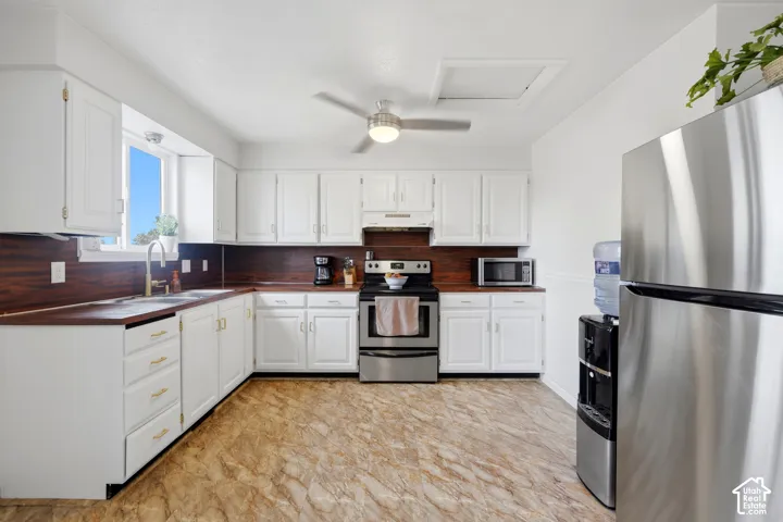 White cabinetry with gold-tone hardware, wood-finish countertops, stainless steel appliances, and a ceiling fan