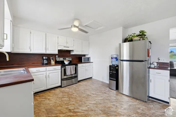 White cabinetry with brushed nickel hardware, stainless steel appliances, wood-finish countertops, wood-finish backsplash, and patterned flooring