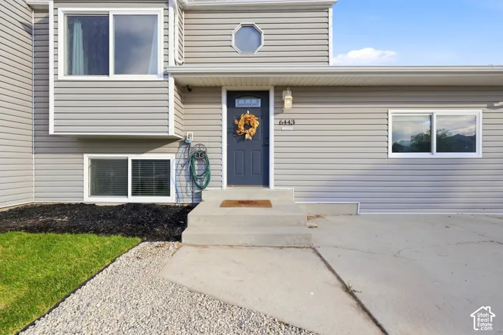 Gray horizontal siding exterior with a dark blue entry door, concrete steps, and a gravel and grass front yard