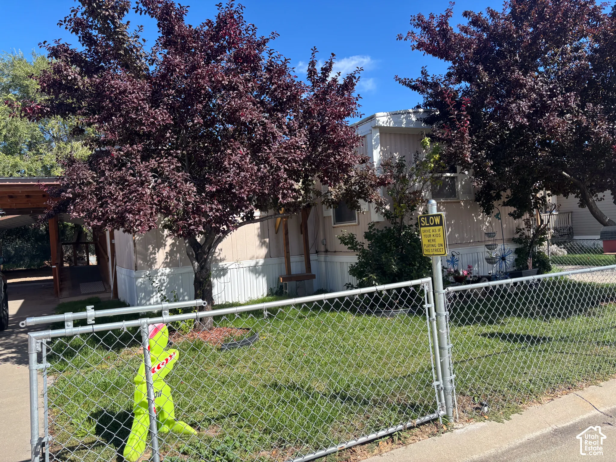 Chain link fence surrounding a grassy area with mature trees and a covered entry