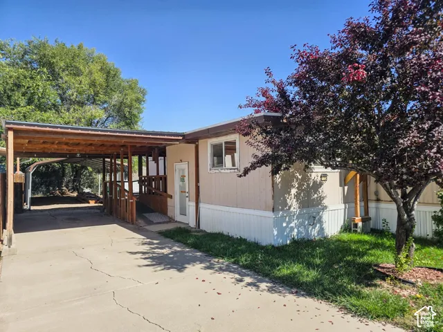 Exterior featuring a covered carport, concrete driveway, wood ramp access, and mature landscaping