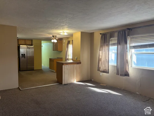 Open-concept living area featuring a kitchen with wood-finish cabinetry, a stainless steel refrigerator, and a ceiling fan