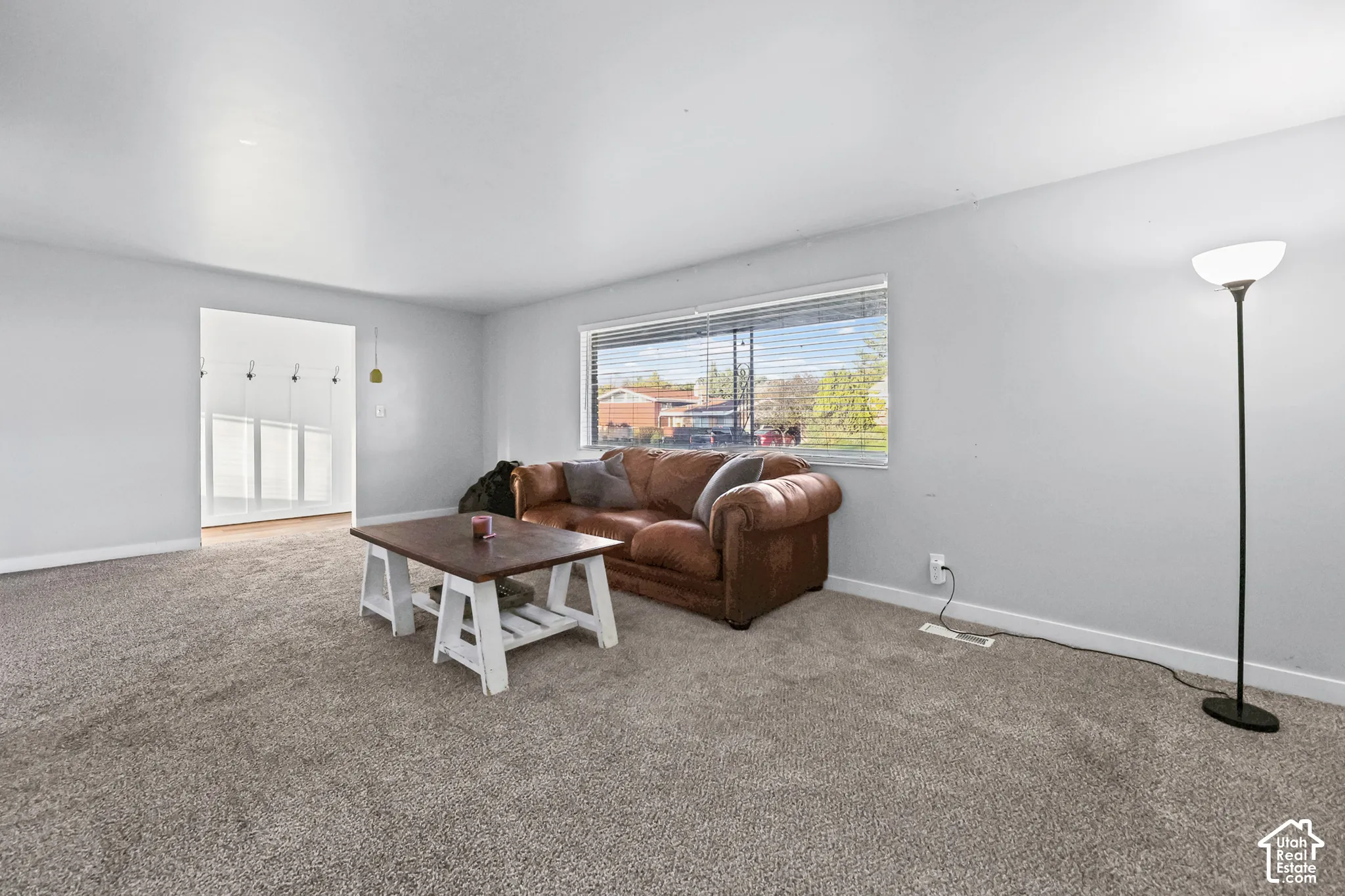 Neutral wall color, carpeted flooring, large window with blinds, and wide doorway opening