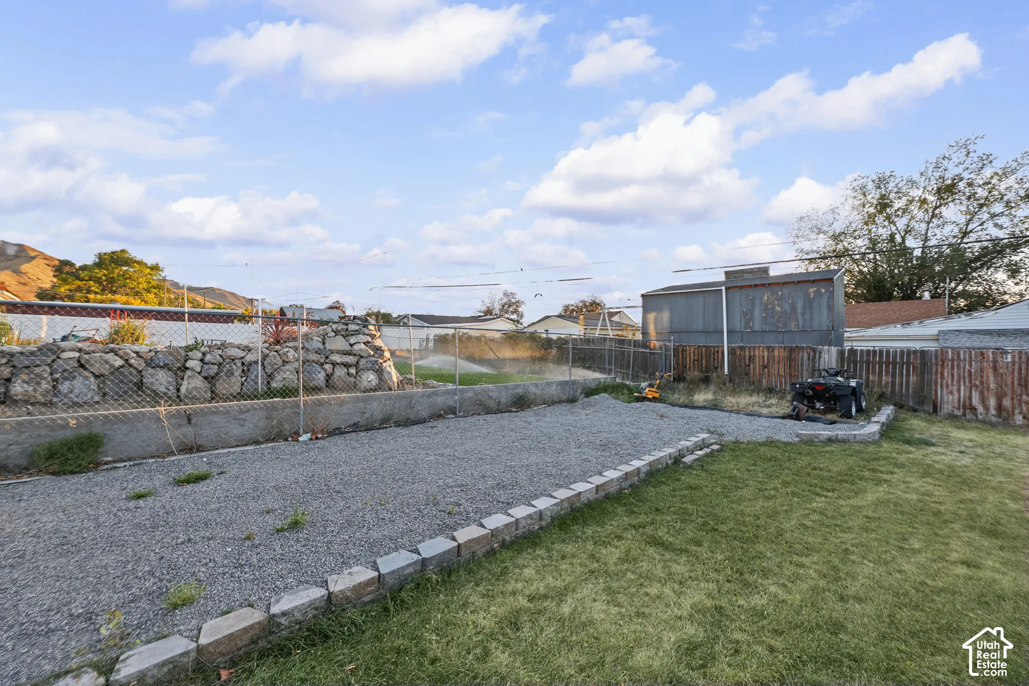 Expansive outdoor space featuring a gravel area, a grass lawn, and a block retaining wall