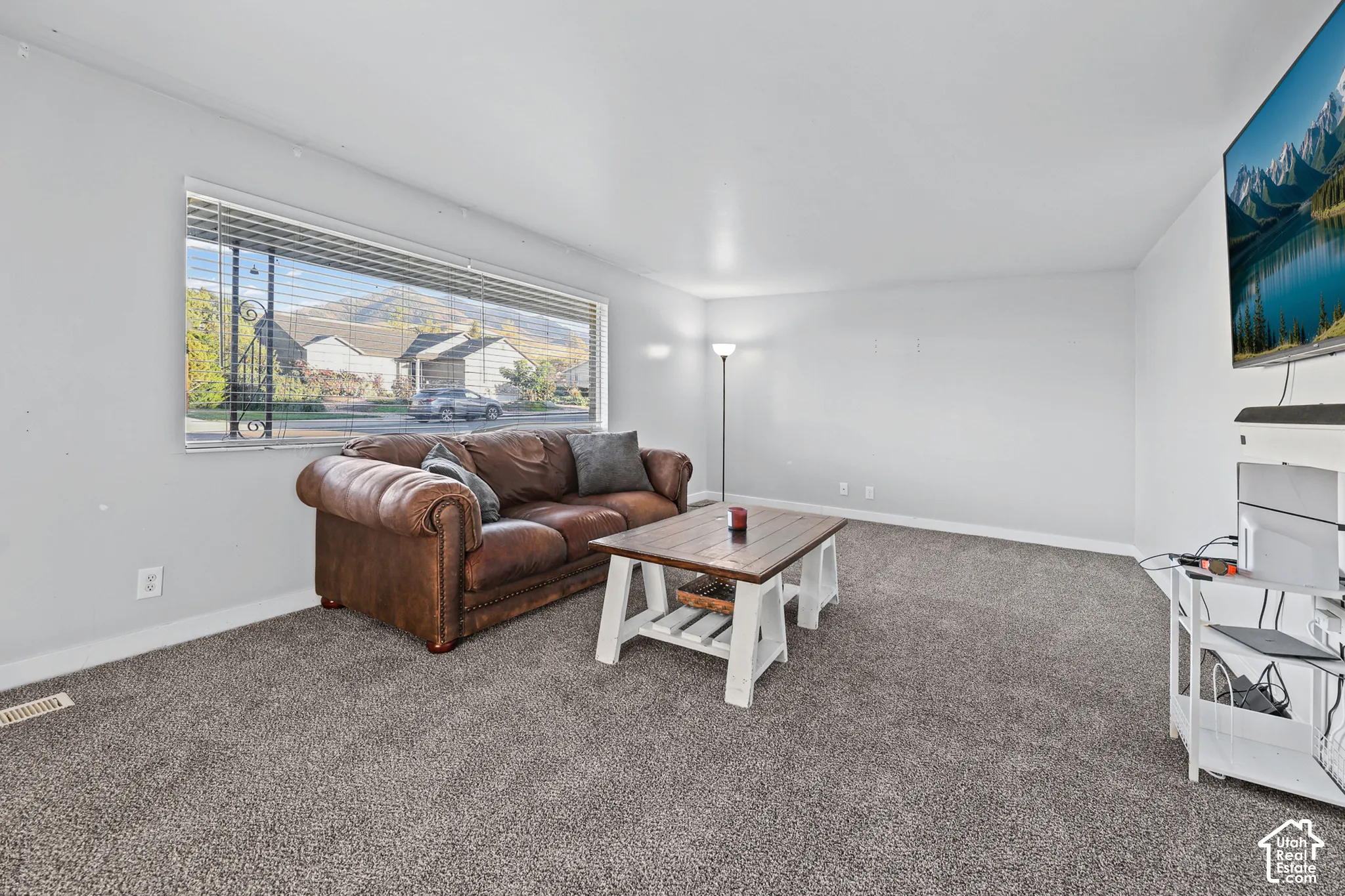 Spacious living area featuring neutral carpeting and a wide window with horizontal blinds