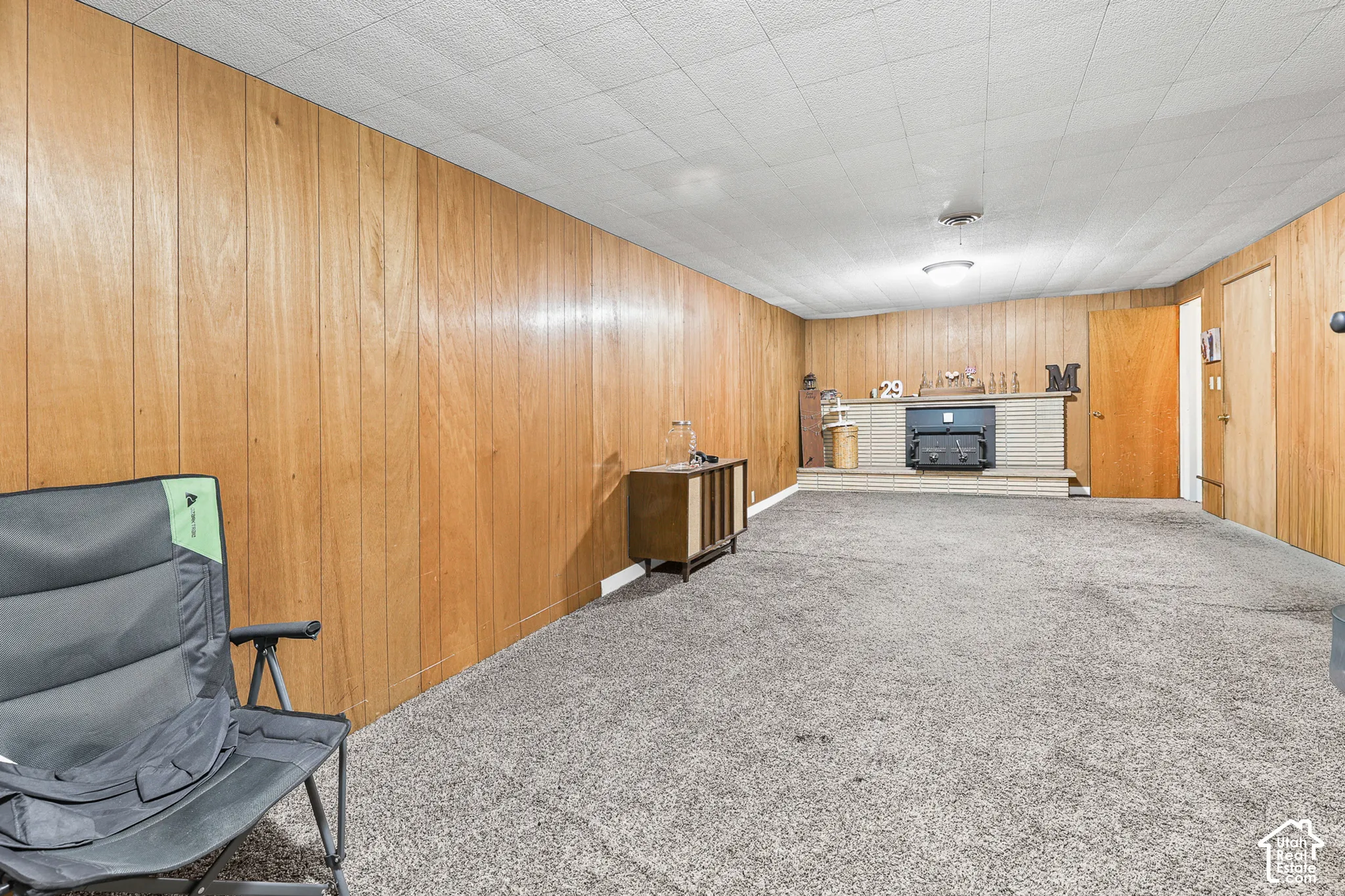 Wood paneling accents a room with gray carpeting and a white acoustic ceiling