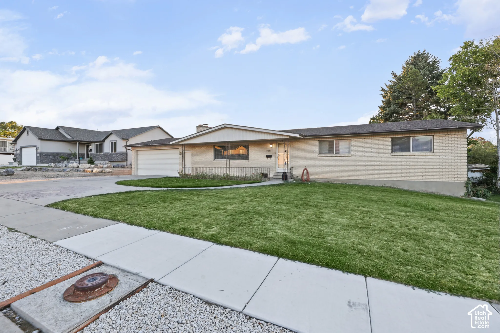 Brick exterior with a gabled roofline, attached garage, concrete driveway, and front lawn
