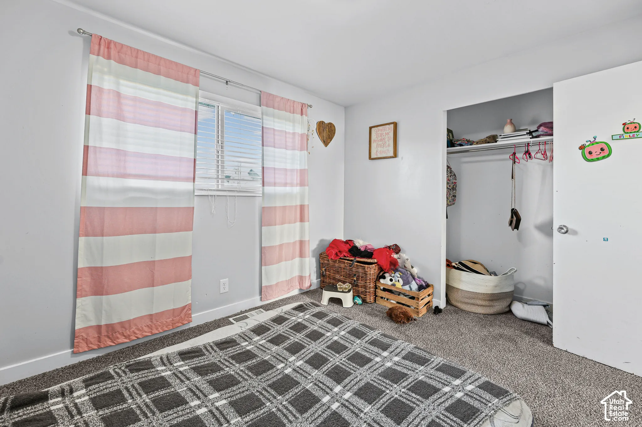 Carpeted flooring, single window with blinds, and an open closet with shelving and a hanging rod