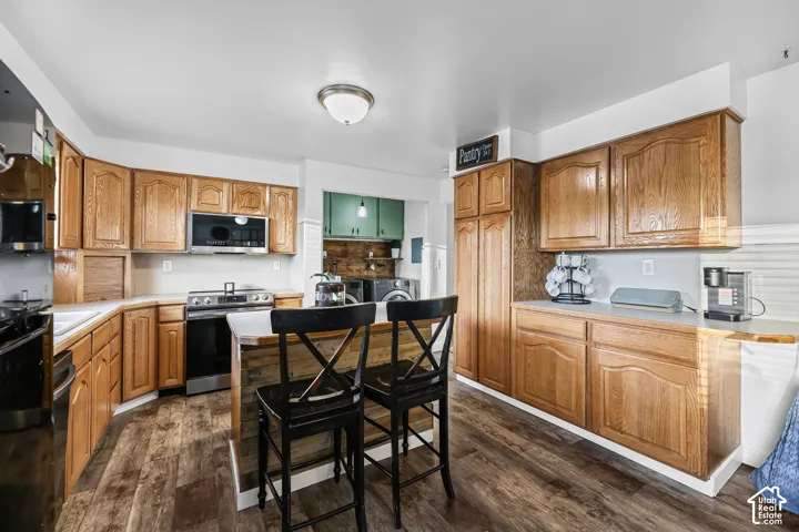 Wood-finish flooring, wood cabinetry, stainless steel range and microwave, and a central island with countertop
