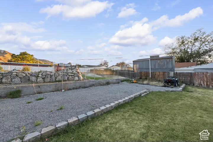 Expansive outdoor space featuring a gravel area, a grass lawn, and a block retaining wall