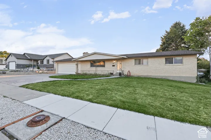 Brick exterior with a gabled roofline, attached garage, concrete driveway, and front lawn