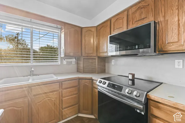 Wood-finish cabinetry, stainless steel microwave, black electric range, double basin sink, and ample countertop space