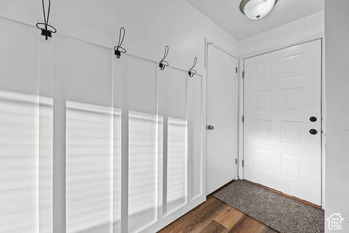 Wood-finish flooring with a paneled wall featuring coat hooks, a flush mount ceiling light, and a white entry door with black hardware