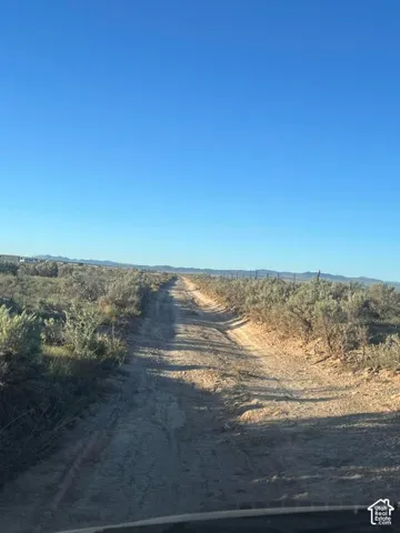 Expansive open terrain with a visible dirt road, featuring sparse vegetation and distant mountains under a clear sky
