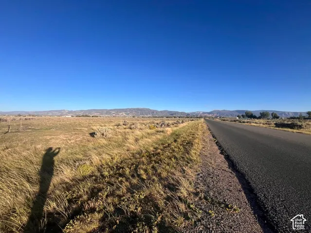 Expansive open land with a paved road, bordered by natural vegetation and distant mountains under a clear sky